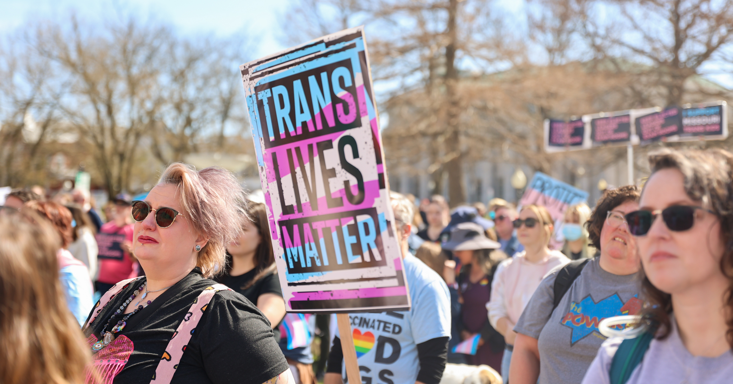 A sign that says "Trans Lives Matter" is held in the air at a protest in Jefferson City for trans rights.